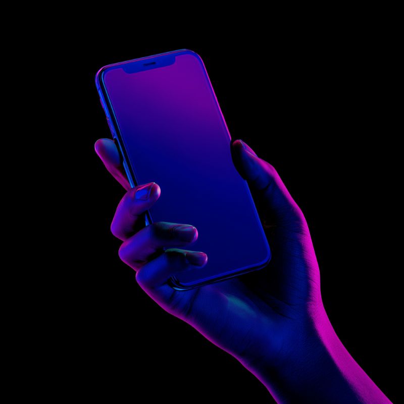 Neon-lit hand holding smartphone against black backdrop